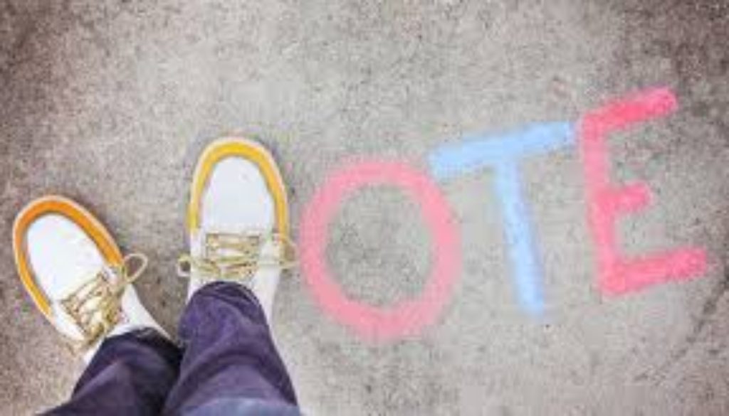 An image of some feet over the word vote chalked on the pavement